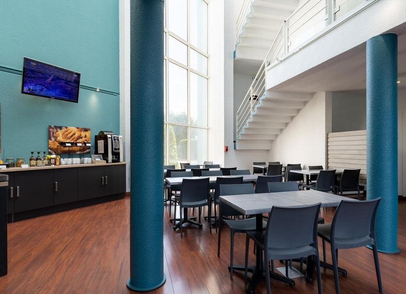 Kyriad Eco Lille Sud - Noyelles Godault dining area with tables, chairs, tall windows and blue columns