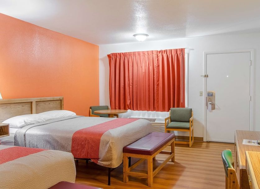 Motel 6 Madras OR room with two beds, orange accent wall, red curtains, and seating area in Madras