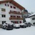 Pension Sonnalp in Ortisei, snowy alpine guesthouse exterior with balconies and parked cars