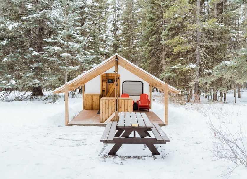 Sundance By Basecamp in Kananaskis, a tiny cabin in snowy forest with picnic table and chairs