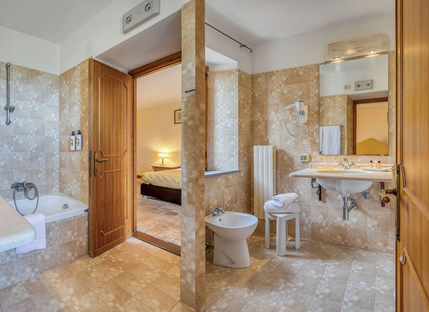 Relais La Fattoria bathroom with bathtub, bidet, sink and open door to bedroom in Passignano sul Trasimeno