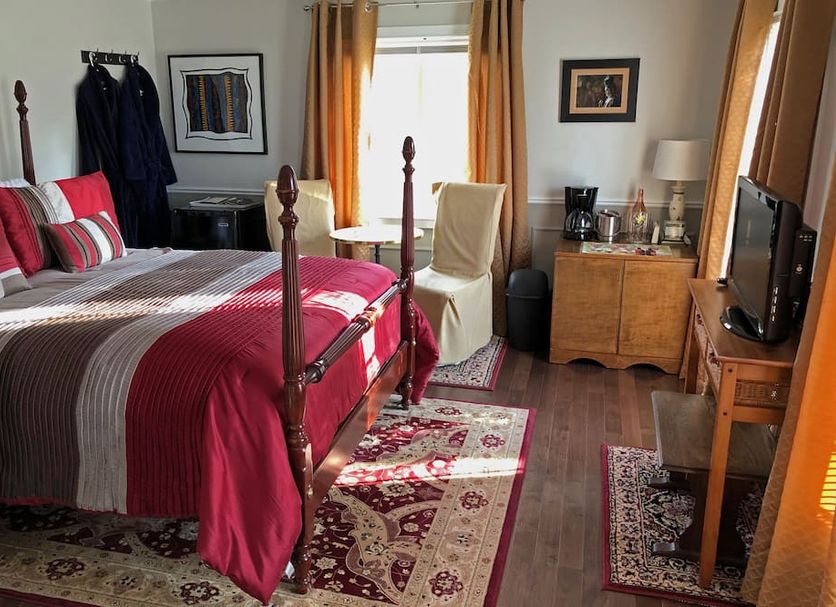 Butler Creek House room in Niagara-on-the-Lake with a four-poster bed, TV, dresser and patterned rugs.