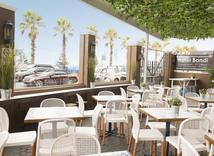 Hotel Bondi, Sydney outdoor terrace with tables, chairs, palm trees and oceanfront view