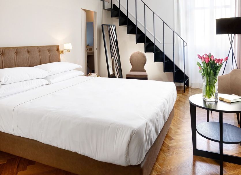 Splendor Suite Rome bedroom with mezzanine loft, wood-beamed ceiling, staircase, and window light