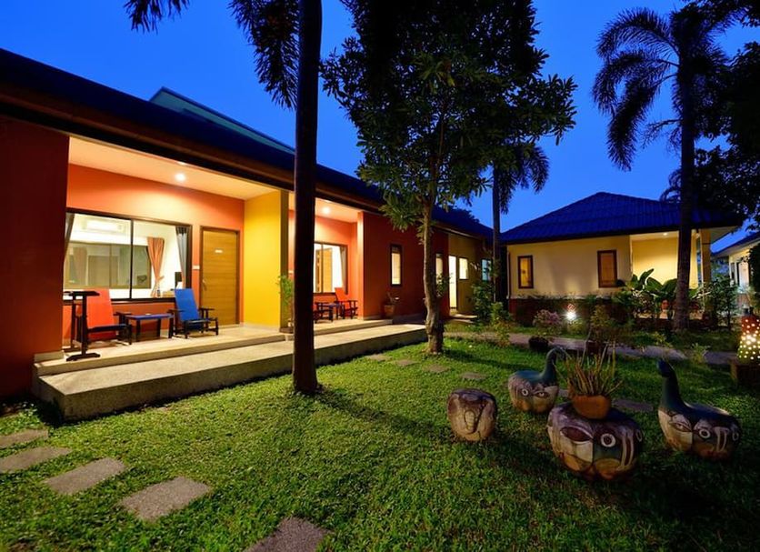 Happy Cottage in Chalong with bungalow rooms, lit patio seating, and a landscaped garden at dusk