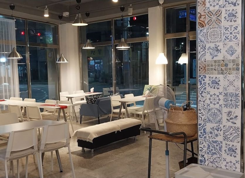 Pohang Youngildae Guesthouse lounge with white tables, chairs, pendant lights and large windows in Pohang