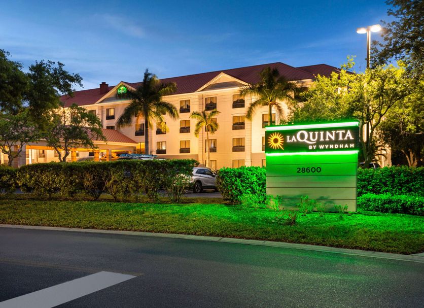 La Quinta Inn & Suites by Wyndham Bonita Springs Naples N. exterior at dusk with palm trees and lit sign