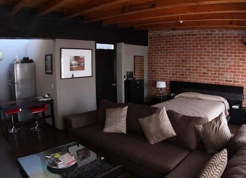 Hotel del Vasco in Zacatecas: rustic room with brick accent wall, dark sofa, bed, and kitchenette