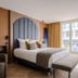 1.75 Paris La Source in Paris hotel room with upholstered headboard, bench, and tall windows