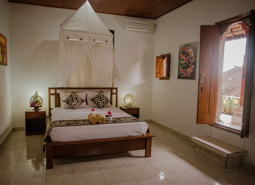 Artha Dewata Home Stay in Ubud bedroom with wooden bed, canopy netting, and open window view