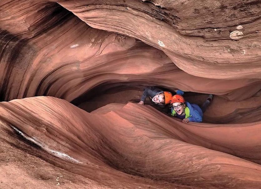 High Desert Inn, Salina: two people in helmets navigating a narrow red sandstone slot canyon