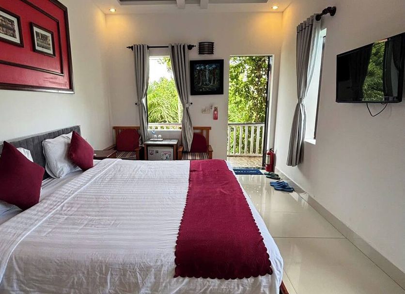 Red House Homestay - Villa, Hoi An: bright bedroom with king bed, balcony doors, and wall-mounted TV