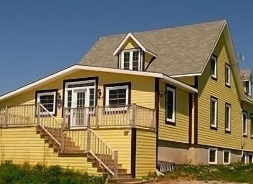 Gîte Au Coin De La Berge in Perce, yellow gîte with wraparound deck and staircase
