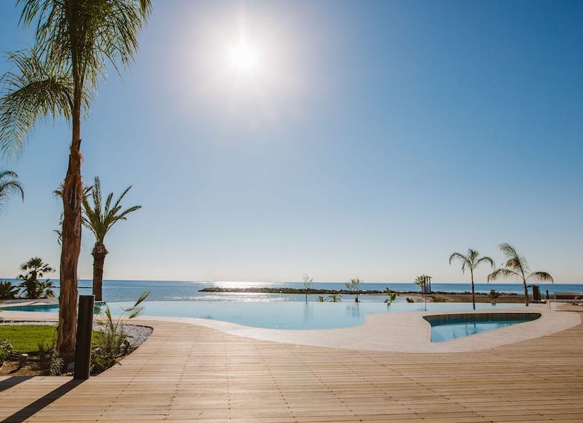Lebay Beach Hotel in Oroklini with a sunlit infinity pool and sea view beside palm trees