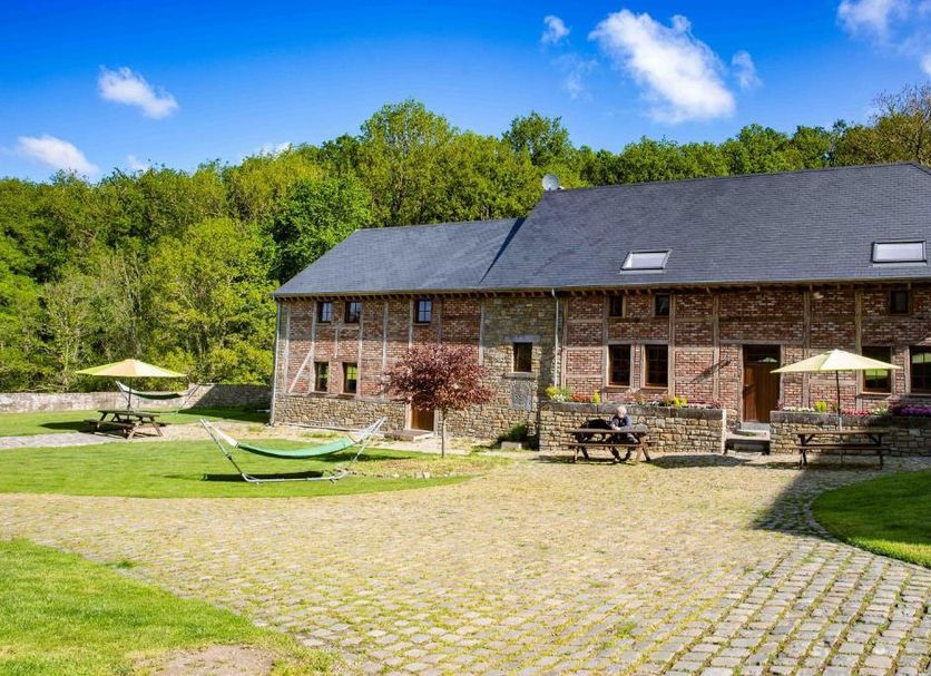 Ferme de Leuze in Somme-Leuze with brick lodge, patio tables, and hammocks on a grassy courtyard