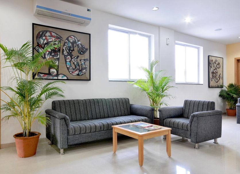 Hotel De Ecobiz Ahmedabad lounge with striped sofa, armchair, coffee table, potted plants and wall art