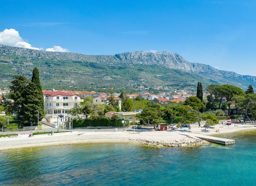 Hotel Riva in Kastela with a seaside beach, clear blue water, and mountain backdrop