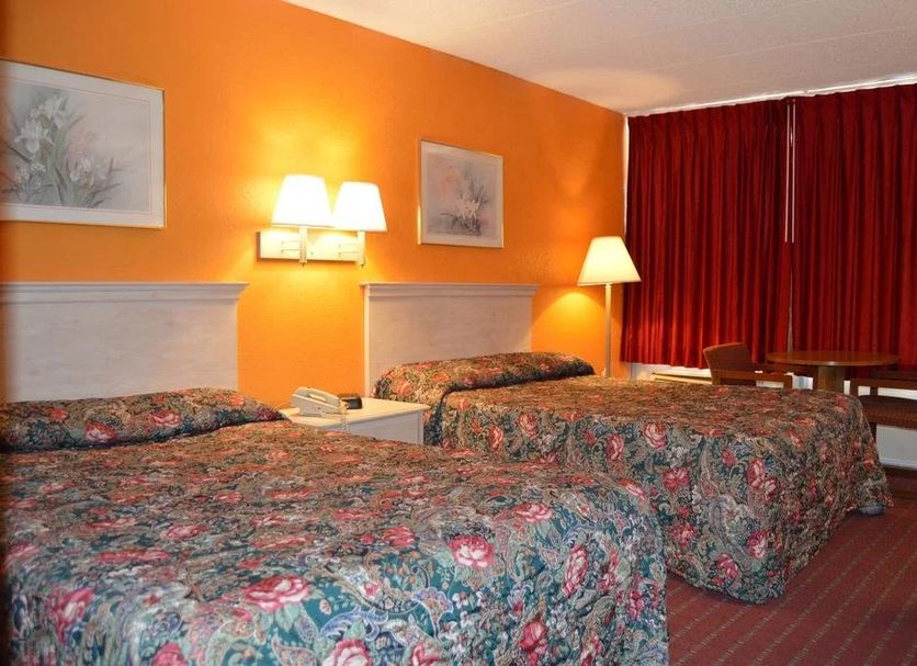 Travelers Inn Dayton guest room with three floral beds, orange walls and red curtains