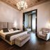 Hotel De la Ville, Riccione guest room with king bed, armchair, tufted bench, chandelier and dark wood floors
