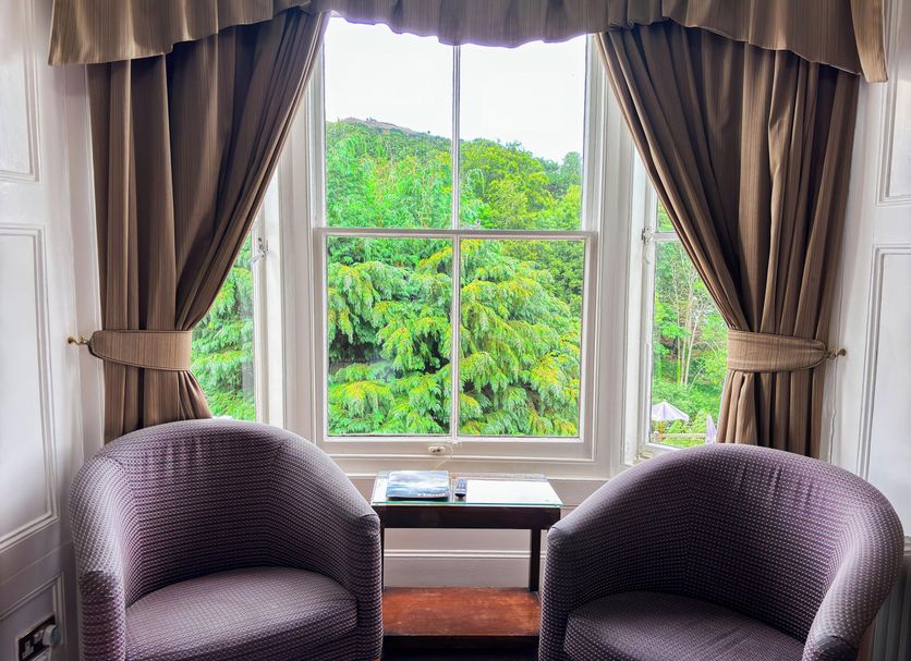 The Hand Hotel Llangollen by Compass Hospitality room with two chairs and a large window to lush green trees.