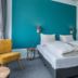 Villahotel Vlissingen room with twin beds, teal accent wall, yellow chair and window curtains in Vlissingen