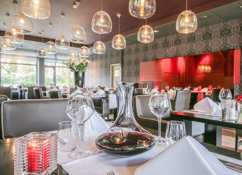 Fletcher Hotel Landgoed Huis te Eerbeek restaurant with set tables, hanging lights and red wall decor in Eerbeek