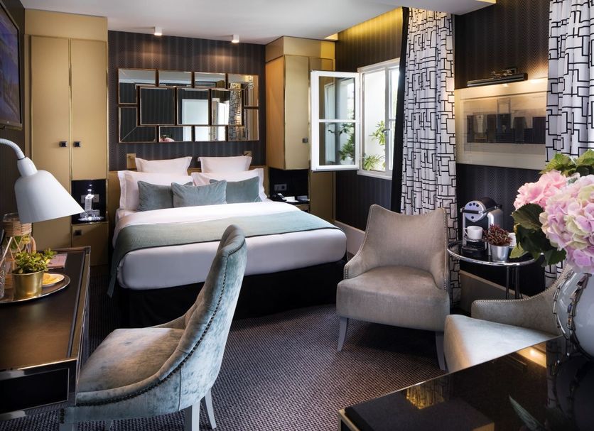 Hôtel Baume in Paris guest room with open window, upholstered chair, and bed with mirrored headboard