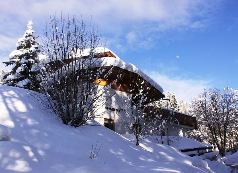 Garni Biancaneve in Ronzone, snow-covered chalet-style hotel on a hillside under blue sky