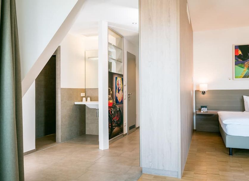Hotel Trezor in Singen: modern guest room with bed, open bathroom area, and colorful wall art