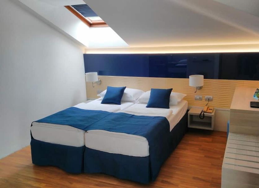 Hotel Abbazia in Lignano Sabbiadoro guest room with twin bed, skylight and blue accents
