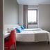 B&B Hotel Milano-Monza room with two twin beds, red chair, desk, and wall-mounted TV in Monza.