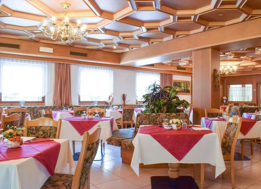 Hotel Scoiattolo in Falcade dining room with red tablecloths, floral chairs and ornate ceiling lights