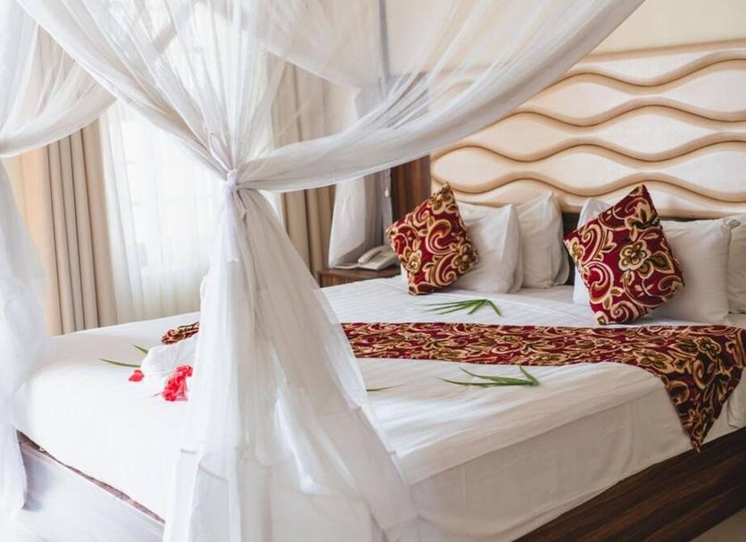Antonio Garden Hotel Zanzibar room with canopy bed, white curtains, and patterned pillows