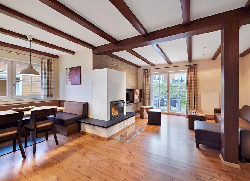 Nürburgring Ferienpark living area with fireplace, wood beams, dining nook and balcony doors in Nuerburg