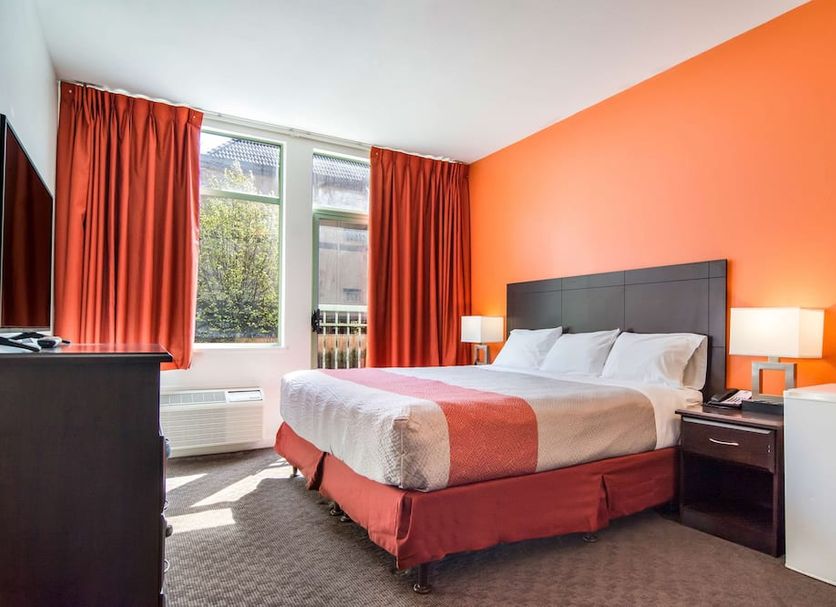 Motel 6 Surrey BC guest room with king bed, orange accent wall and window with red curtains