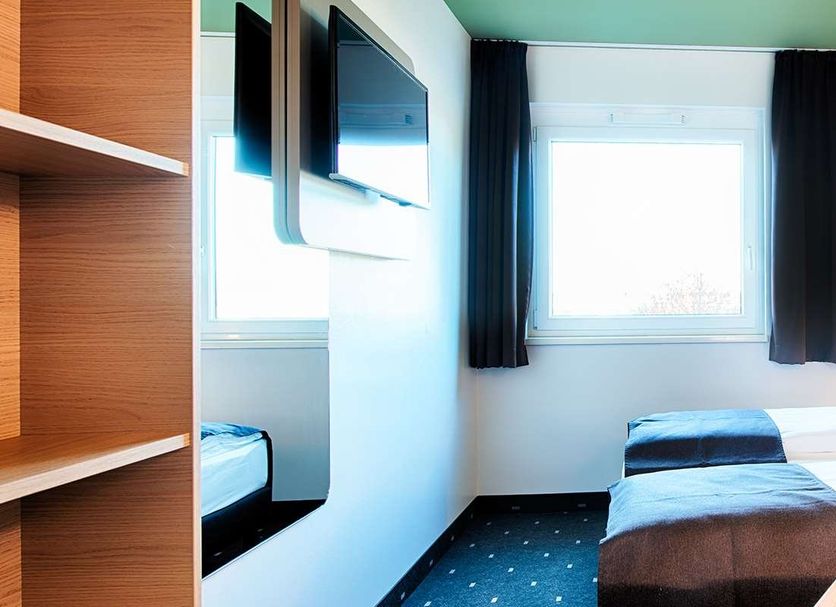 B&B Hotel Baden-Airpark in Rheinmunster guest room with twin beds, window, wall-mounted TV and colorful mural