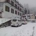 Hotel Sumit Kausani beside a snowy mountain road with parked vans and hillside buildings in Kausani
