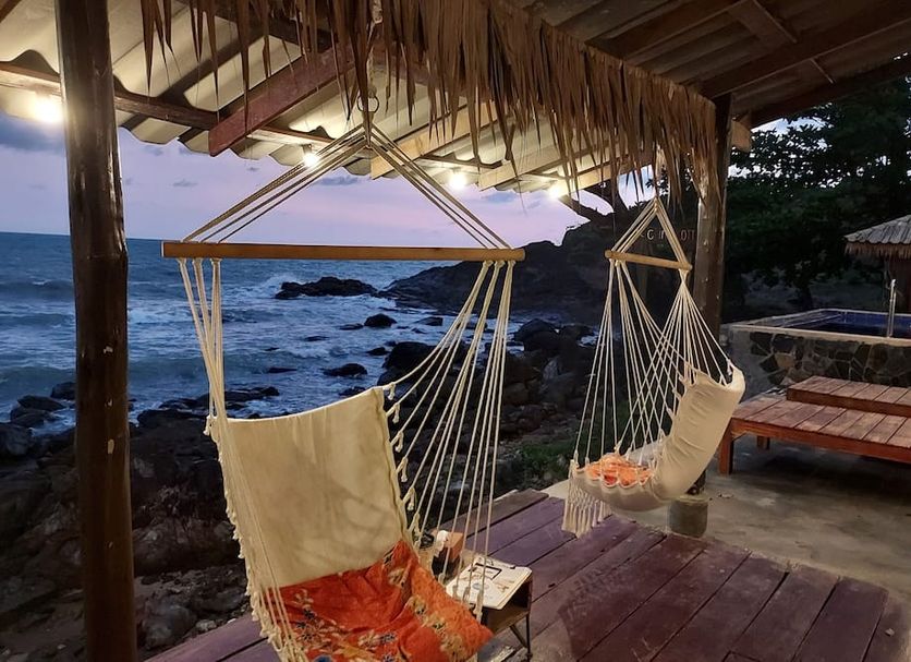 Cliff Cottage in Ko Chang with hanging chairs overlooking the rocky ocean at sunset