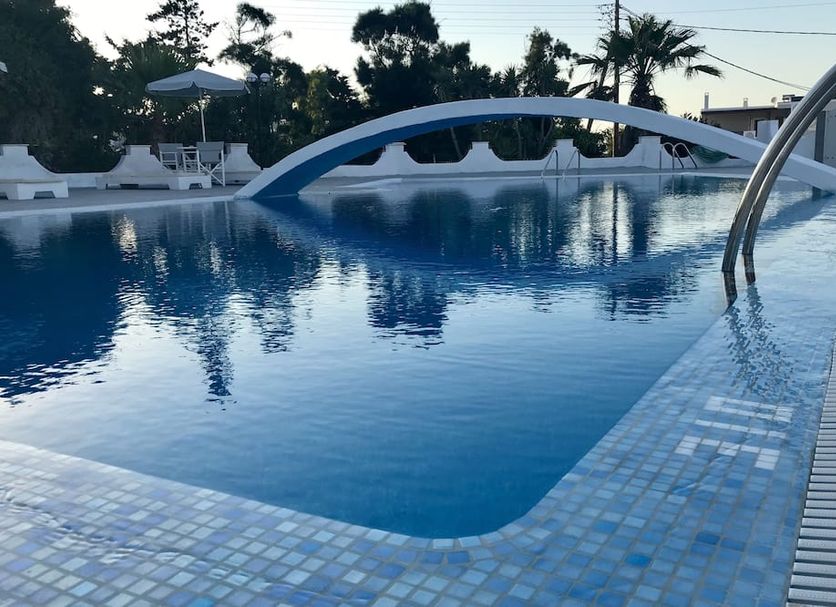 Hotel Lodos in Karterados with a blue outdoor pool and arched bridge at dusk