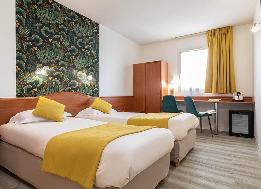 Deltour Hotel Le Puy En Velay guest room with twin beds, desk, window and yellow accents in Le-Puy-en-Velay