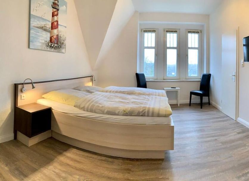 Gästehaus Seewarte Flensburg room with curved bed, lighthouse wall art, and chairs by windows