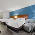 Baymont by Wyndham Tuscaloosa guest room with two beds, blue accent wall, desk and armchair