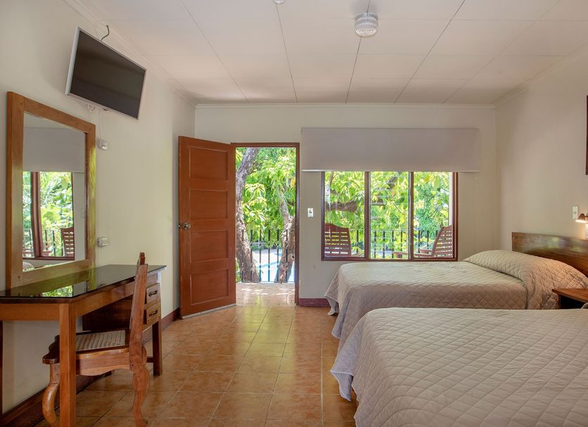 Hotel Boyeros Liberia guest room with two beds, desk, wall TV and balcony view of greenery