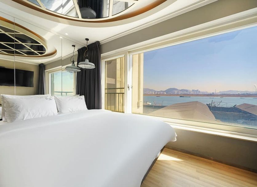 Jk Hotel Busan room with king bed and large window overlooking the sea and distant mountains