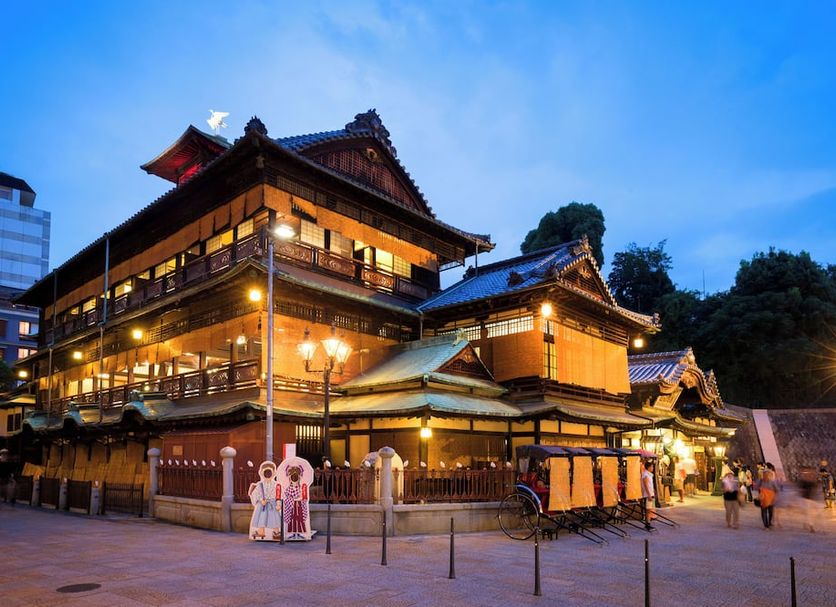 Dogo Grand Hotel in Matsuyama at dusk, showing a traditional Japanese-style exterior lit up at night