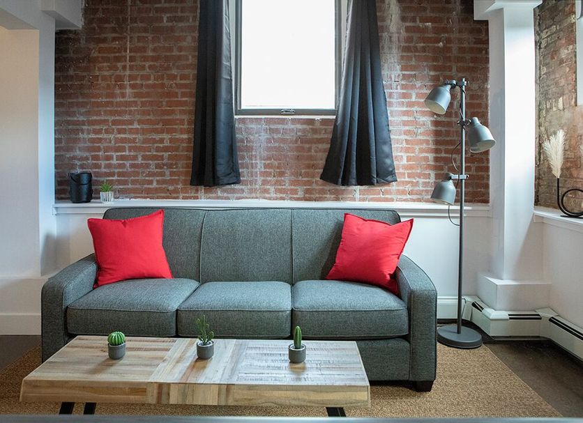 Cameo Hotel and Suites Halifax living area with gray sofa, red pillows, brick wall and wood coffee table