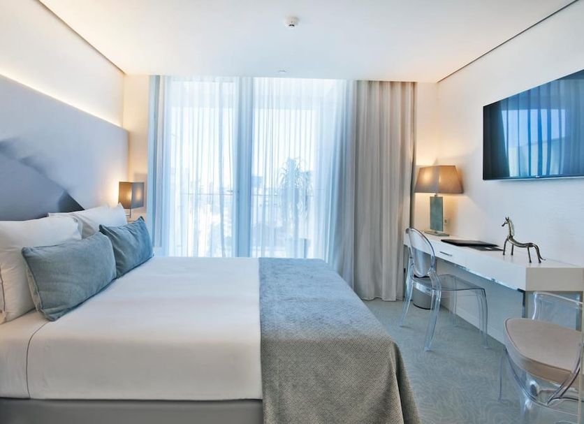 Hotel White Lisboa Lisbon guest room with king bed, desk, wall TV and city view through curtains