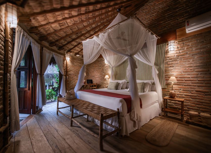 Vila Kalango in Jijoca de Jericoacoara, canopy bed in a rustic brick room with wooden floor and bench