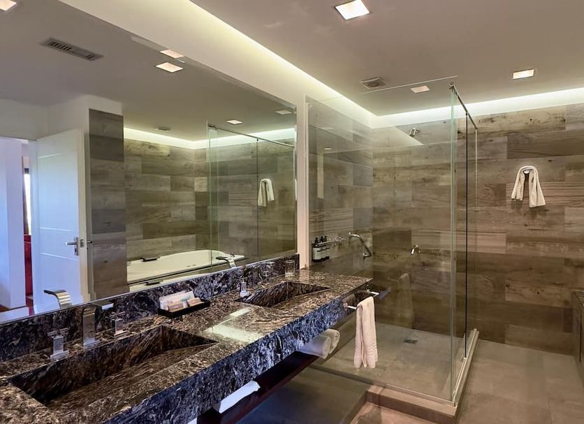 Neper Hotel Cordoba bathroom with double vanity, large mirror, glass shower and stone tile walls