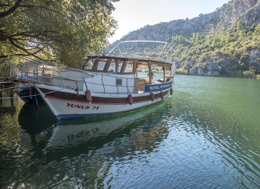 Hotel Riverside boat on a calm river in Dalyan, Mugla, beside forested cliffs